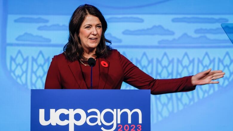 a woman extends her left hand while speaking at a lectern.