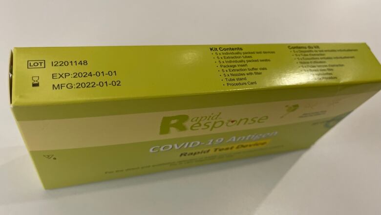 A green COVID-19 rapid response test kit sits on a white table. An expiry date of January 1, 2024 is stamped on the box.