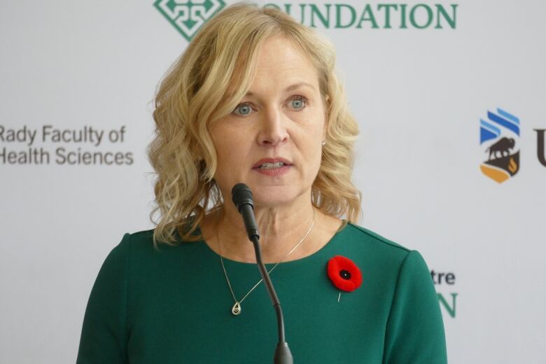 A woman with shoulder-length blond hair in a green shirt and poppy pinned below her left shoulder.