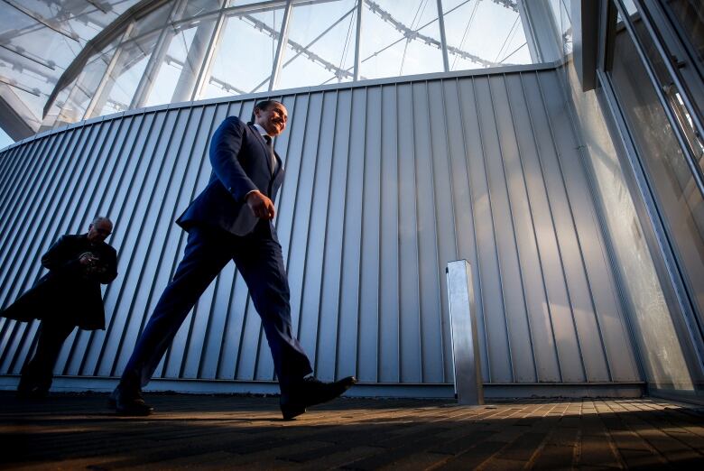 A man in a suit walks past a curved, corrugated metal wall.