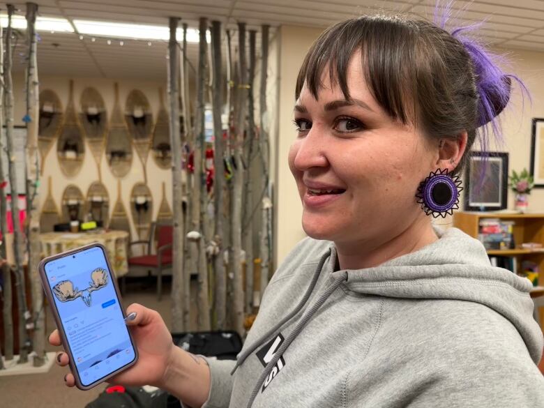 A woman stands holding up a smart phone with an image of antlers on it.