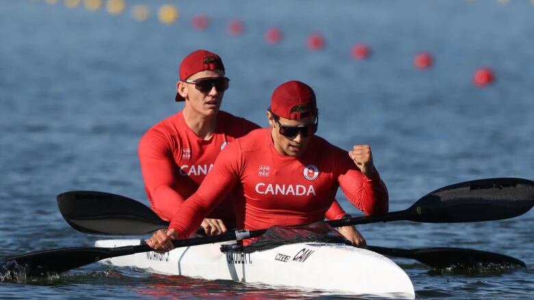 Two paddlers wearing red Canada attire sit on the water in their white watercraft.