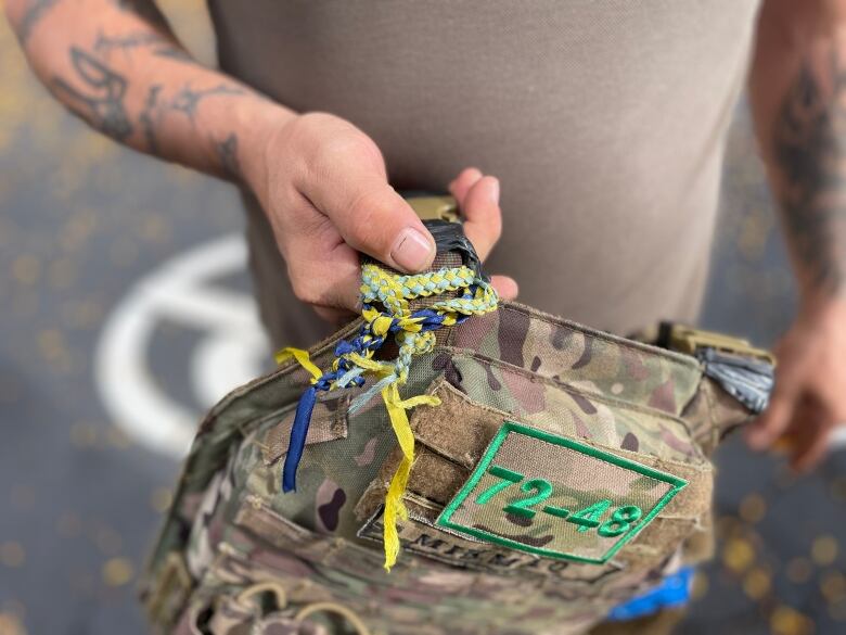 A fatigue coloured backpack with blue and yellow ribbons tied on the straps. 