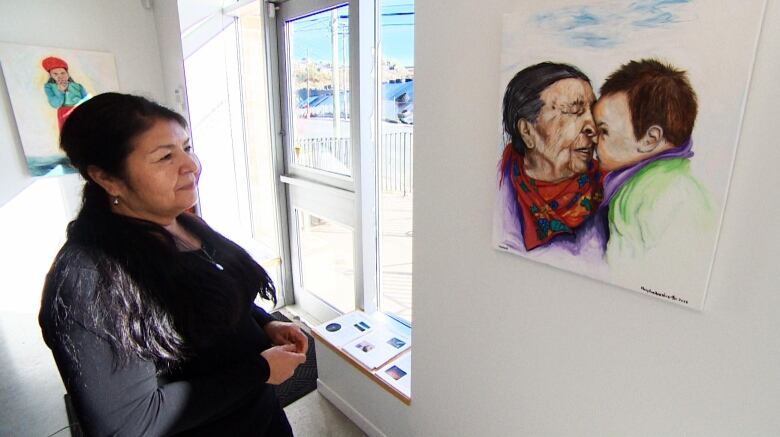 Woman standing in front of a painting of a grandmother and her great-granddaughter. 