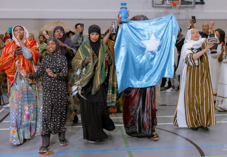 Women in long robes and head scarves walk through a gym.