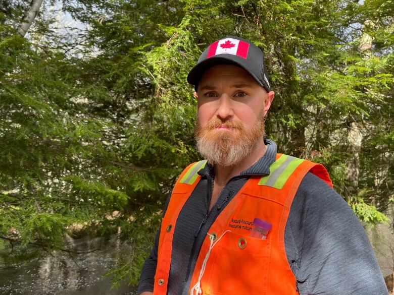 A man wears a hat with a Canadian flag on it and a bright orange safety vest. 