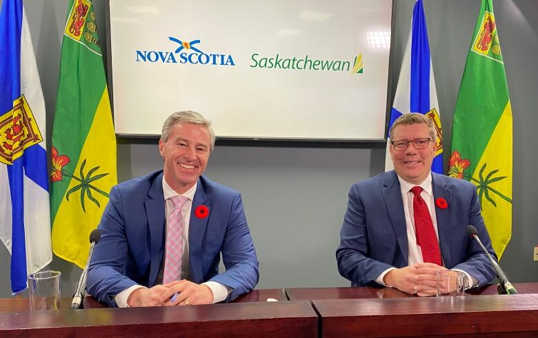 Two men wearing blue suit jackets and ties smiling.