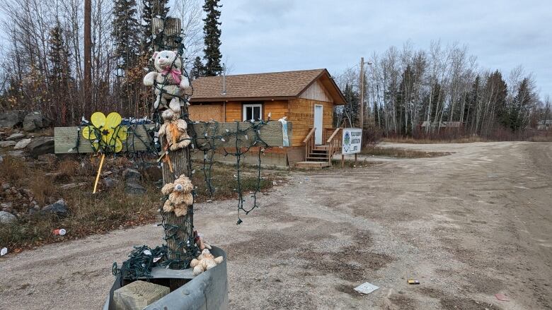 a cross at the edge of a small bridge backgrounded by a Pelican Narrows community building