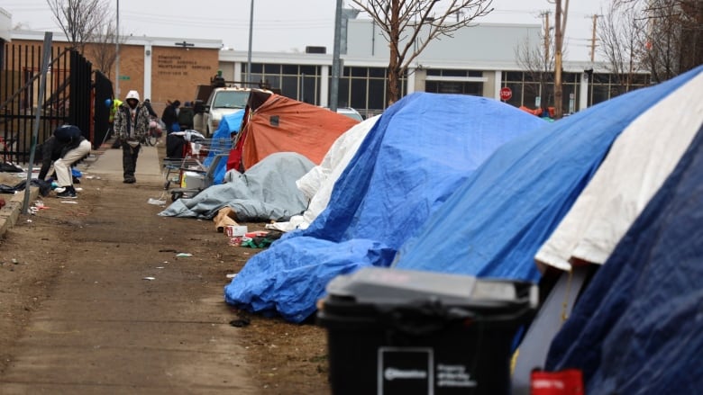 A series of tents set up beside a sidewalk. Some people can be seen on the pathway.