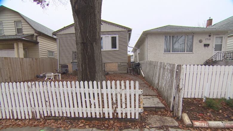 White picket fence surrounds beige home in the fall.