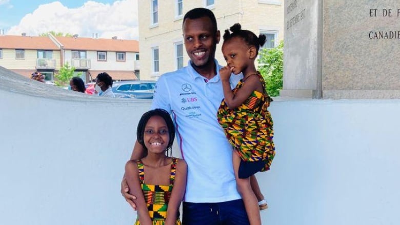 A man poses for a photo outside with two smiling girls.