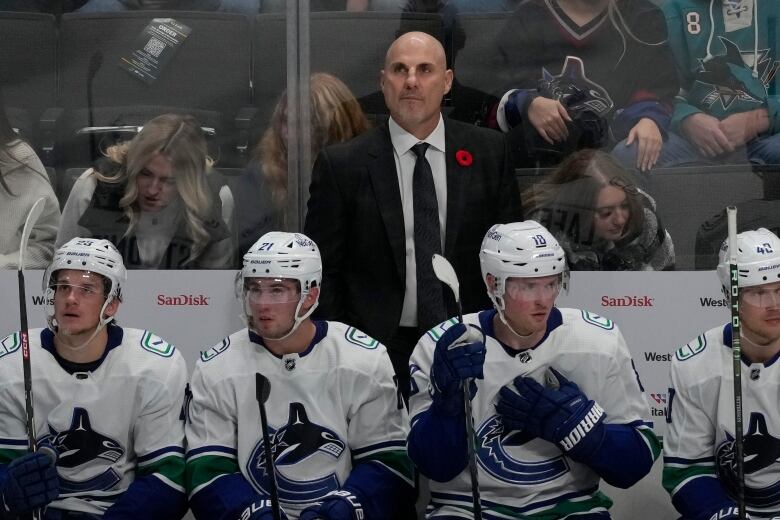 A man in the coaches' box looks on as a line of hockey players sit down.