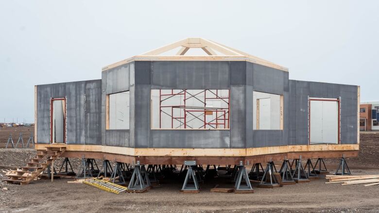 An igloo-ish shapped building on dirt. The building is in the middle of being constructed with an unfished roof and base.