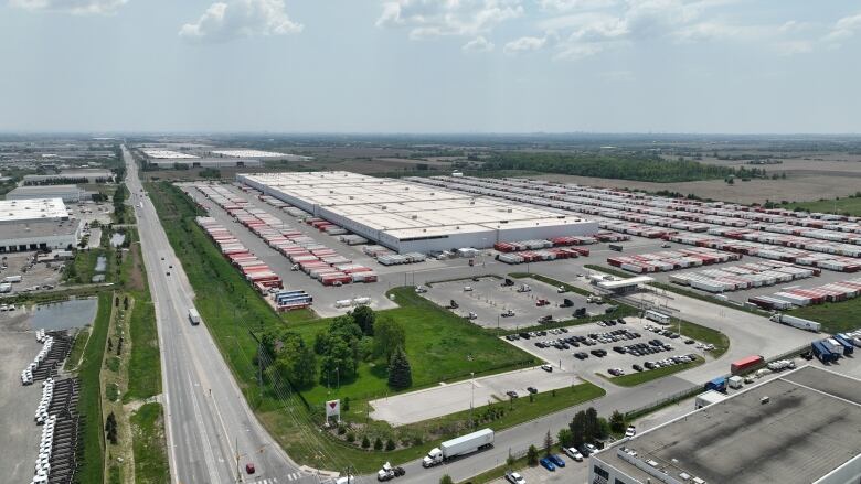 A wide aerial view of a large Canadian Tire distribution centre with many semi-trailers in a parking lot. 