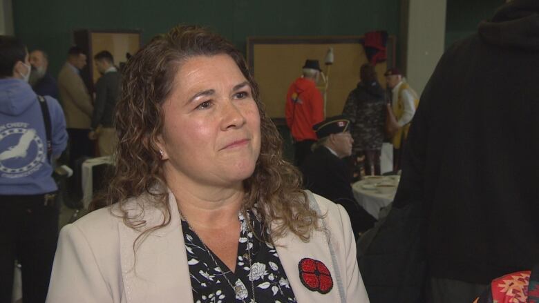 A woman wearing a beaded poppy stands facing forward.