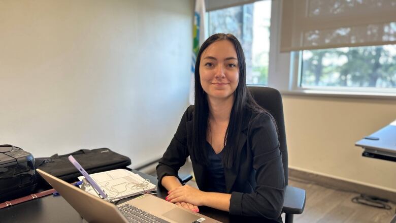 Young woman sitting at a desk in an office in front of a laptop.