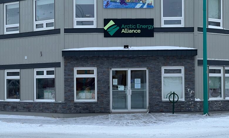 An office building is seen from the outside in winter, with a sign above the door reading, 'Arctic Energy Alliance.'