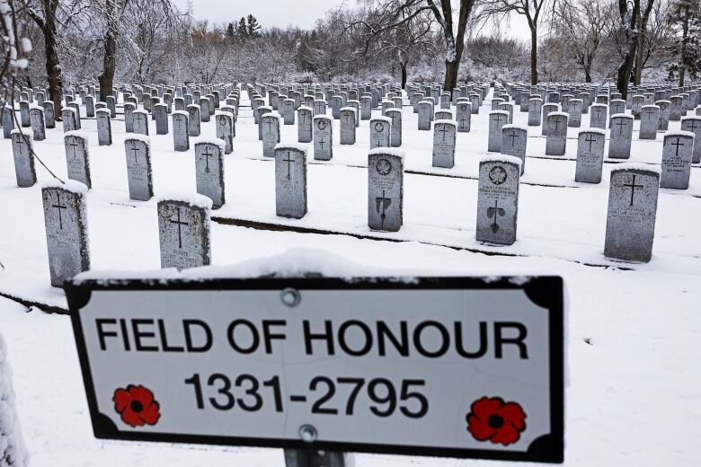 A sign saying Field of Honour is in the foreground with rows of gravestones, surrounded by snow, in the background.