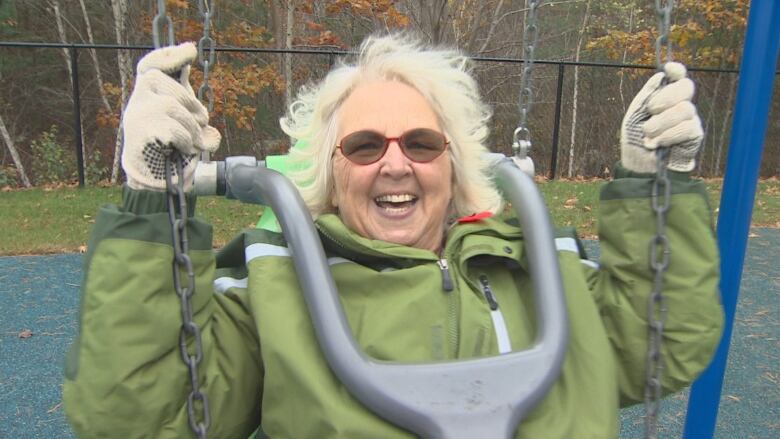 A woman wearing glasses smiles as she swings on an accessible swing set.