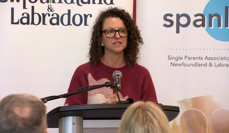 A woman with glasses, wearing a red sweater, standing at a podium. 