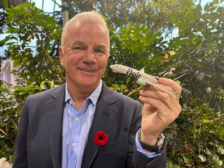 A man wearing a suit holds a miniature model of an airplane. The plane is white with lime green accents, and has the word 'flair' plastered on the side.