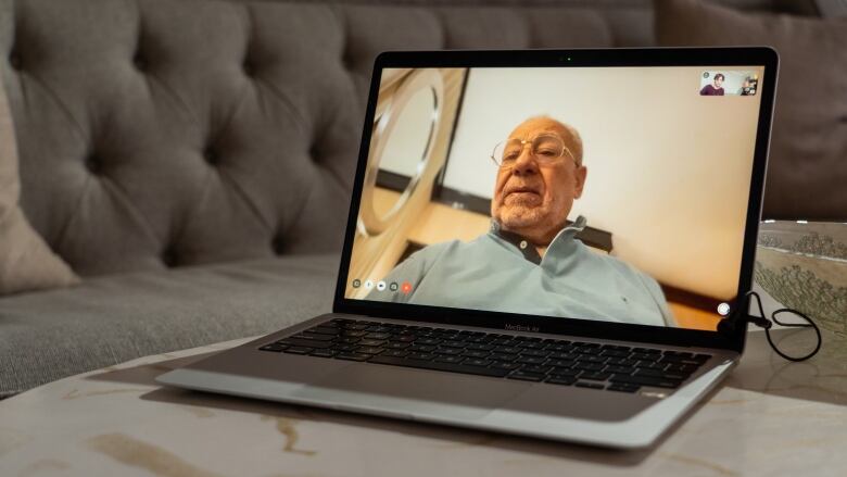 A man appears on a computer screen sitting on a table.