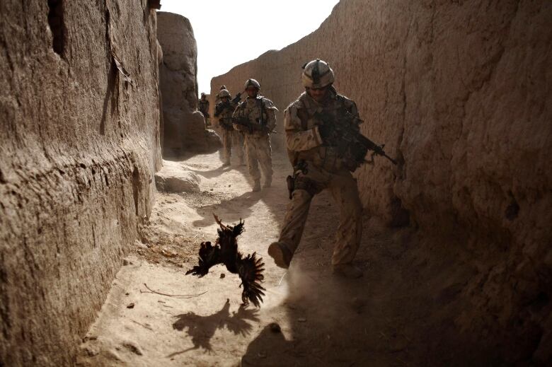 Armed soldiers walk down a narrow passageway between earth walls.