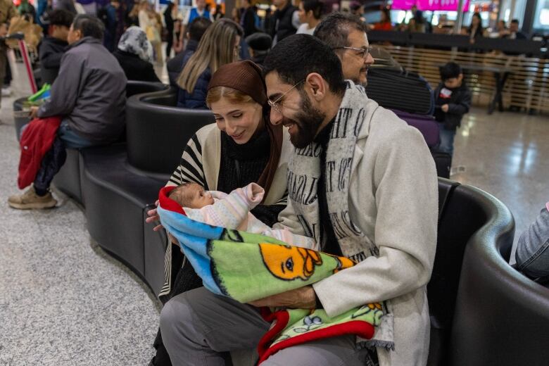 Two people sit holding a baby.