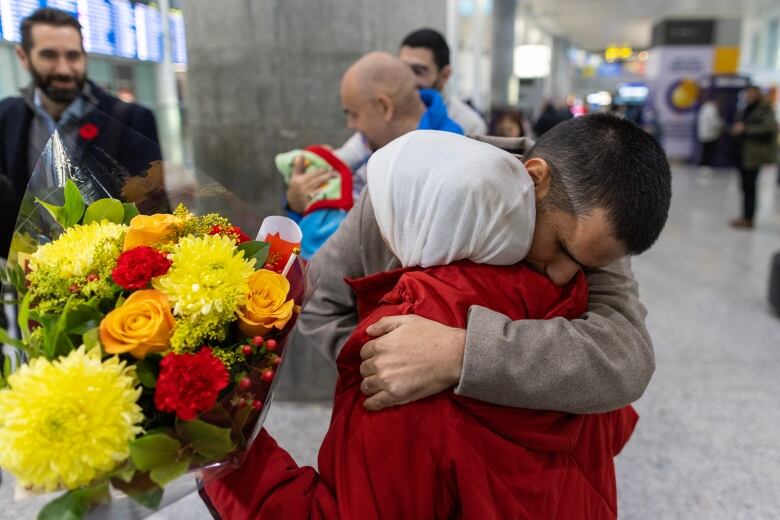 A man hugs his wife who holds flowers.