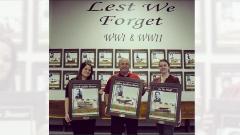 Three people hold framed photos. 