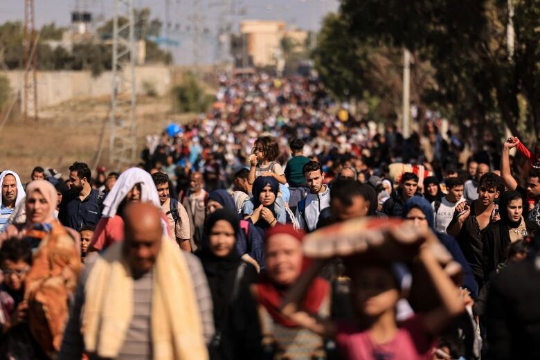 A child sits atop an adult's shoulders as a large convoy of people walk down a road.