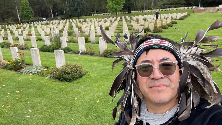 A man wearing a headdress with graves in the background.  