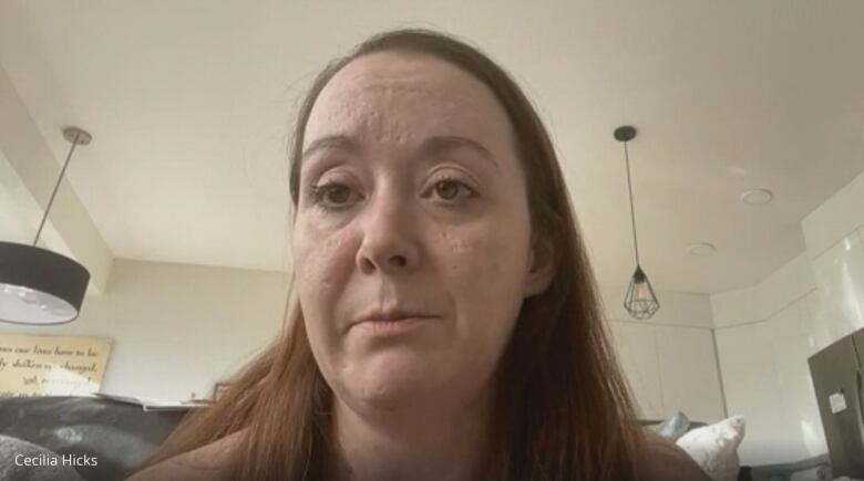 A lady with long brown hair sits in her living room.