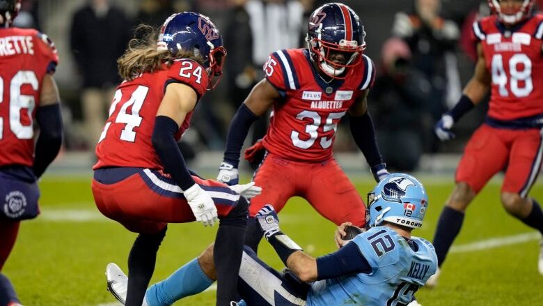 Two football players wearing red gear are seen standing over a fallen opposition player wearing light blue gear.