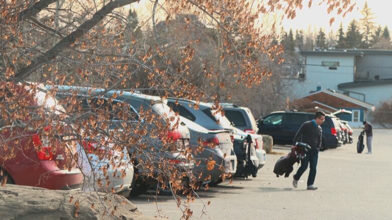 A man walks from his car with his golf bag in his hand.