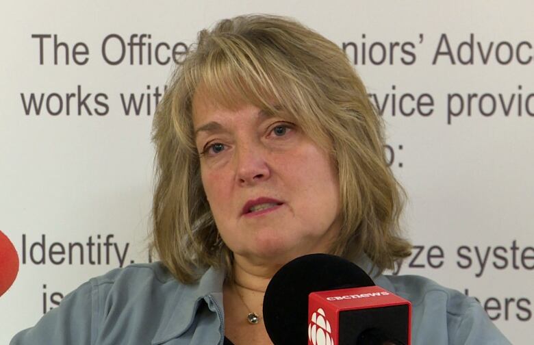 A woman with blond hair sits in front of microphones.