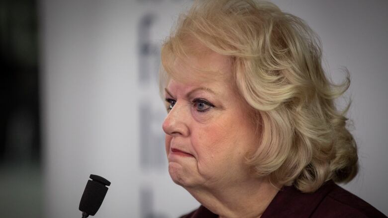 A white woman with short blonde hair scowls while delivering a news conference.