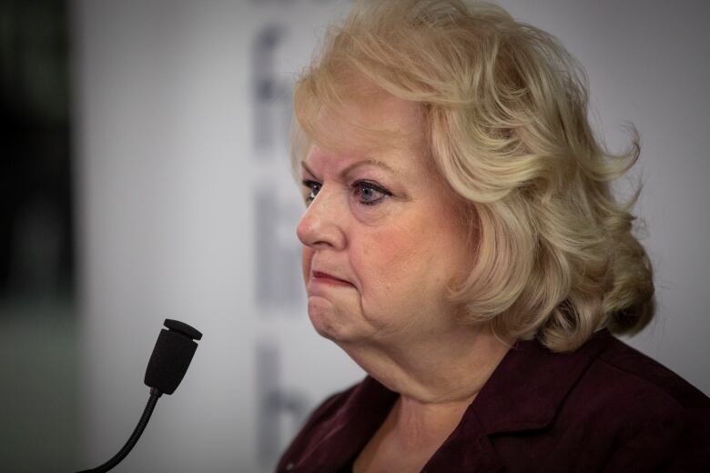 A white woman with short blonde hair scowls while delivering a news conference.