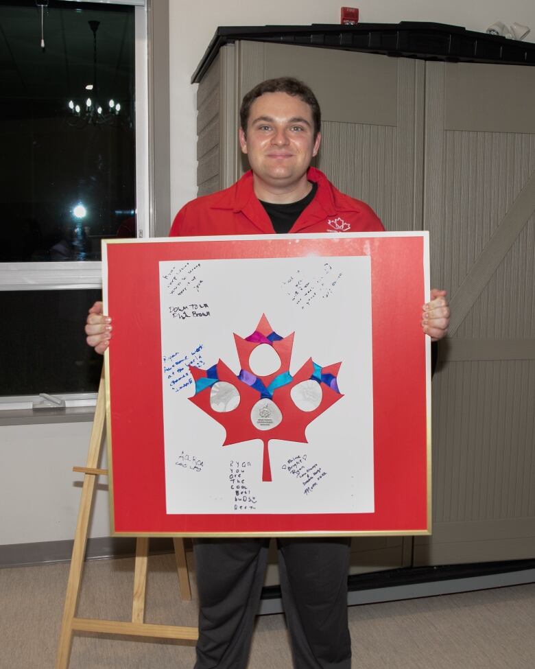 A man holds up a red framed maple leaf, with three medals on it and messages of appreciation.