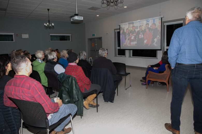 People are seen looking at a presentation in a community centre, on a projection screen.