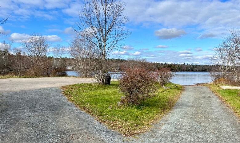 A gravel road and parking lot with a lake in the background.