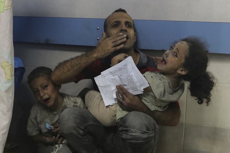 A distraught man holds his two screaming children in the emergency ward of a hospital.