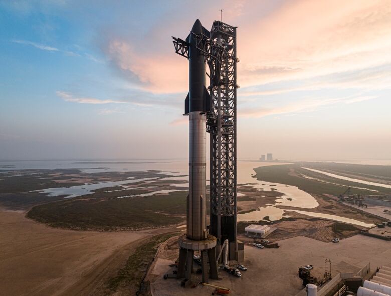 A silver and black rocket is seen sitting on a launch pad near the ocean.