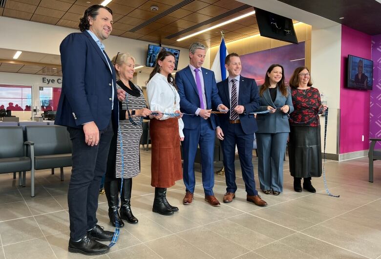 Six people stand in a row holding a ribbon.