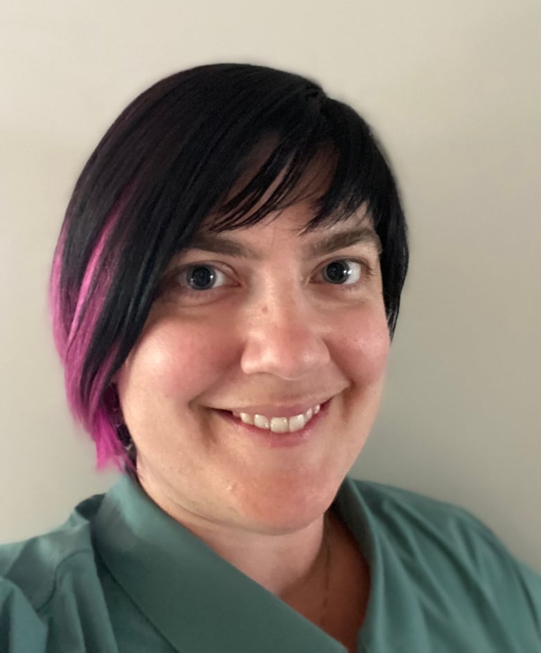 Dr. Cassandra Hoggard smiles as she looks into the camera. She's wearing green scrubs and her dark brown hair streaked with purple.