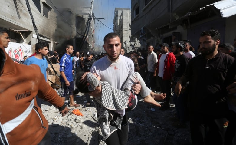 A man in a white shirt carries an injured child in his arms. 