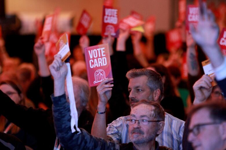 People at a gathering hold up orange cards reading 'Vote Card'.