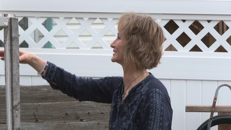 a woman with short hair and a blue shirt waves through a fence