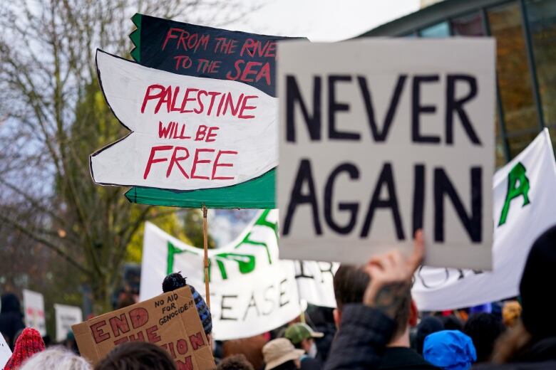 Demonstrators hold up signs that say 'From the River to the Sea, Palestine will be Free' and 'Never again'.