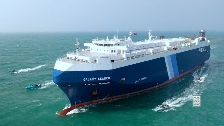 Boats escort a cargo ship at sea.